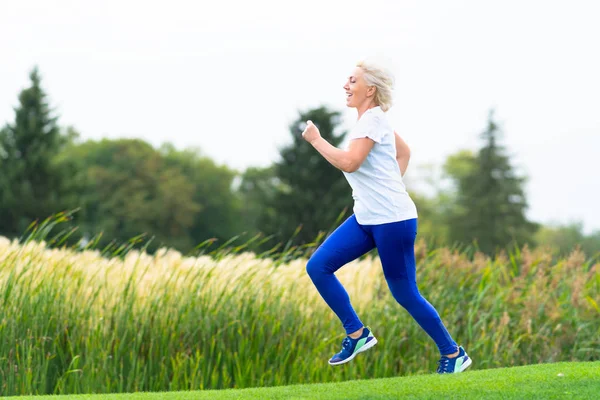 健康とフィットネスの概念にある公園で湖の岸に葦と一緒に実行しているフィット スポーツ熟女 — ストック写真