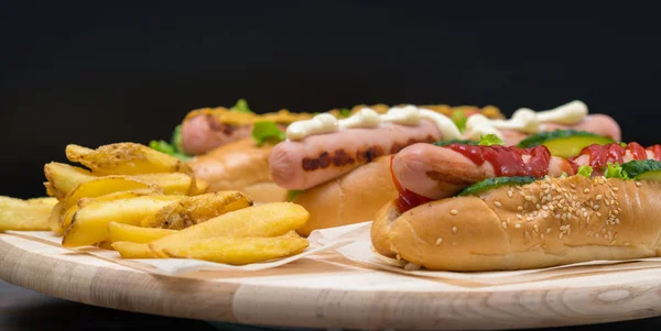 各式特色热狗 配以横幅格式的木板上的油炸薯片搭配不同的侧面辅料和敷料 — 图库照片