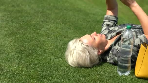 Mujer rubia acostada boca arriba sobre la hierba — Vídeo de stock