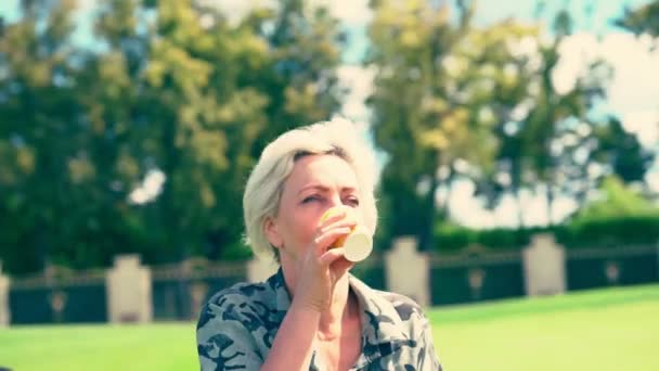 Blond woman outdoors in a park drinking — Stock Video