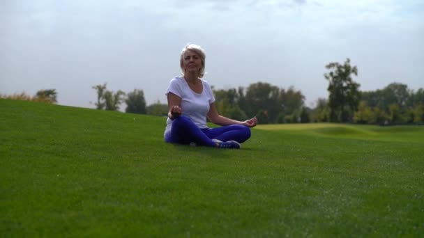 Зрелая Женщина Сидящая Траве Парке Медитируя Спокойной Улыбкой Вращающемся Панорамном — стоковое видео