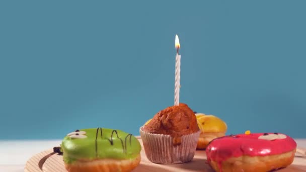 Маффин с горящей свечой и ледяными пончиками — стоковое видео