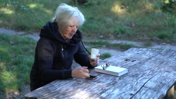 Frau sitzt in einem Park und trinkt Kaffee — Stockvideo