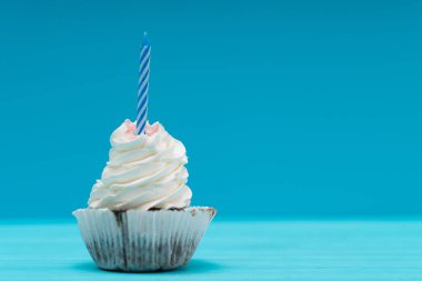 Cupcake döndürdüm buzlanma ve kopya alanı ile mavi üzerinde bir Doğum günü veya yıldönümü kutlamak için sönük mum ile