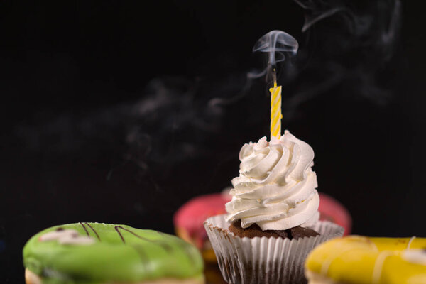 Iced cupcake with smoking candle surrounded by colorful glazed donuts in a low angle view