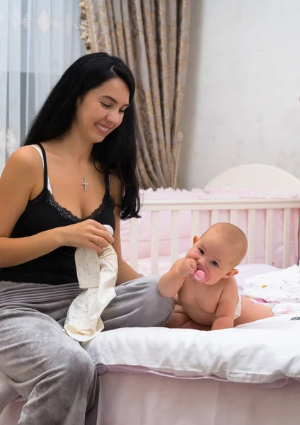 A smiling, young mother and her happy baby in a pink bedroom scene.