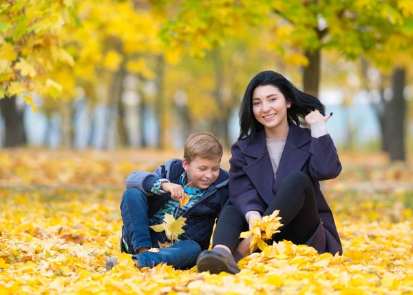幸せで コンテンツの母と息子の座っていると黄色の紅葉の中で都市公園で遊ぶ — ストック写真