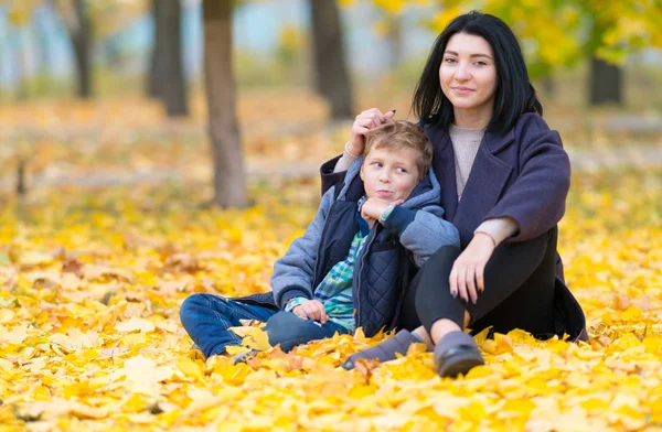 一个快乐的母亲和儿子坐在公园里黄色的落叶中 — 图库照片