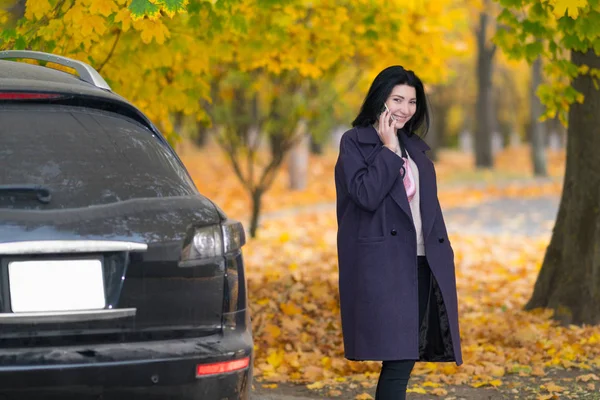 年轻女子在一个五颜六色的秋园里 走出车 用手机聊天 — 图库照片