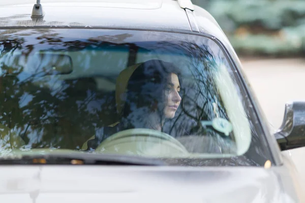 女性ドライバー座って待っている真剣な表情を持つ側の窓の外を見つめて自分の車にフロント ガラスを通して見た — ストック写真
