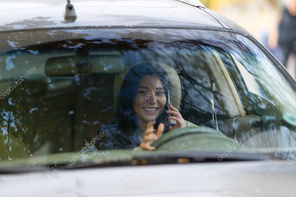 Happy woman chatting on a handheld mobile phone while driving her car viewed through the windscreen with reflections on the glass