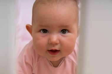 Sevimli küçük bir bebek kız onun karyolası meraklı bir ifade ile kameraya barlar ile bakarken kafa vurdu