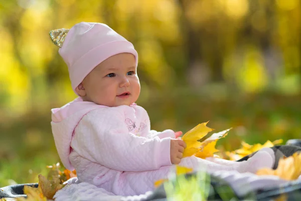 在公园里 一个穿着粉色衣服的婴儿坐在秋天的灯光下 坐在黄色的落叶中 — 图库照片