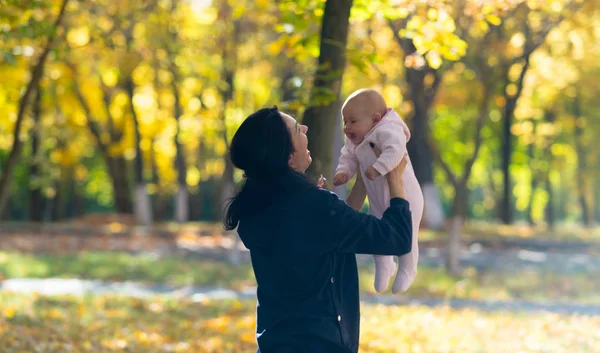 在一个明亮的秋天公园场景中 一个笑着快乐的母亲和她的孩子一起玩耍 — 图库照片