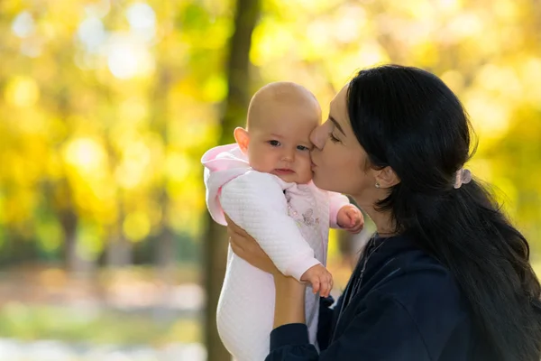 母の愛情を込めて明るい秋の公園シーンで頬に彼女の赤ちゃんにキス — ストック写真