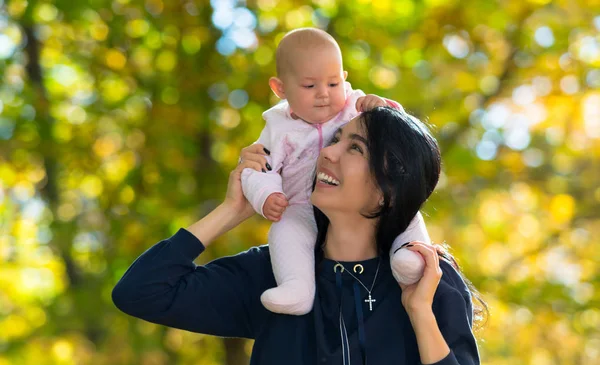 幸せな若い母の貯金箱カラフルな黄色の秋の公園を通って彼女の肩の彼女の赤ん坊の娘をバックアップ — ストック写真