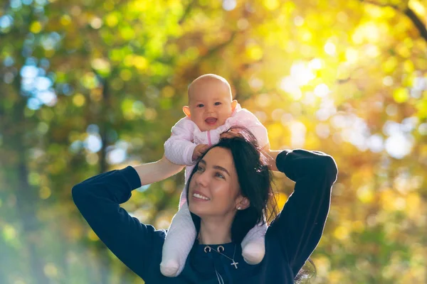 秋の森で彼女の母の肩の上でピギーバック乗りを楽しんで 笑っているの快活な小さな赤ちゃん女の子 — ストック写真