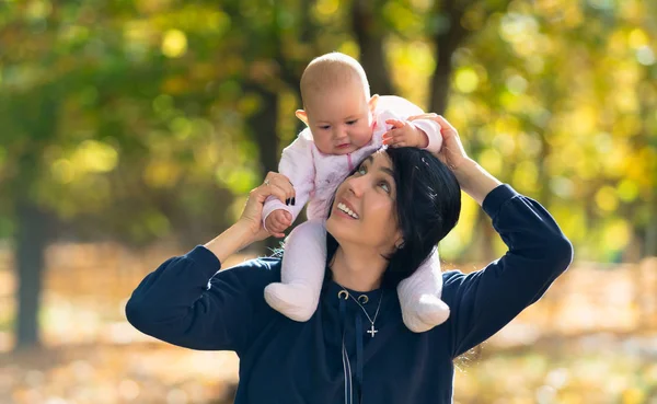 日当たりの良いカラフルな秋の公園で遊んでいる間顔つき片肌笑顔は彼女に彼女の赤ん坊の娘を持つ若い母親 — ストック写真