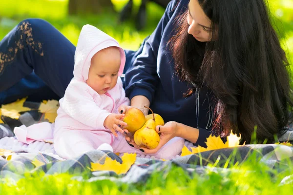 年轻的母亲向她的宝贝女儿展示新鲜的秋苹果 他们在公园里的草地上一起放松 在近距离的视野中 — 图库照片
