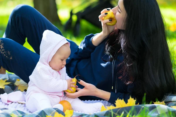 在户外公园或花园的毯子上 母亲和小女儿在一张近距离的家庭画像中吃着新鲜的落苹果 — 图库照片