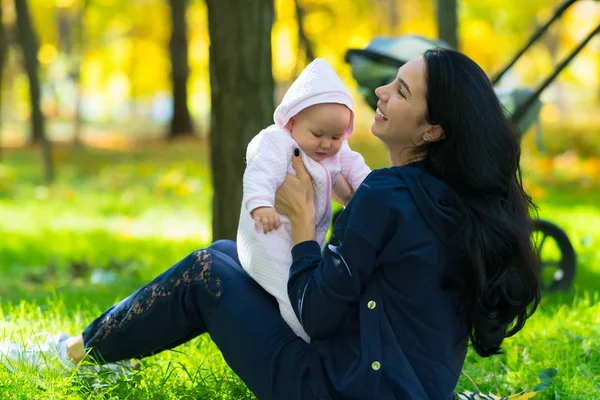 快乐的年轻妈妈在秋天的公园里和一个可爱的女婴在草地上玩耍 — 图库照片