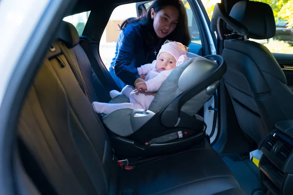 車両の反対側から見た車の後部座席に赤ちゃん用の椅子に彼女の赤ん坊を入れて母 — ストック写真