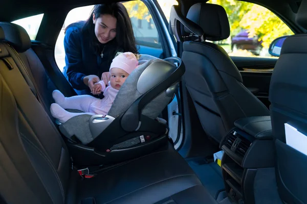 年轻的母亲站在婴儿旁边 坐在婴儿座椅上 倒在黑色内饰的汽车后座上 — 图库照片