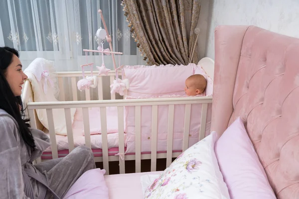 A happy, young mother and baby in a pink bedroom scene with crib.