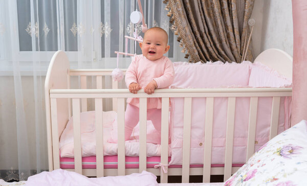 A happy, laughing baby in crib in pink bedroom scene.