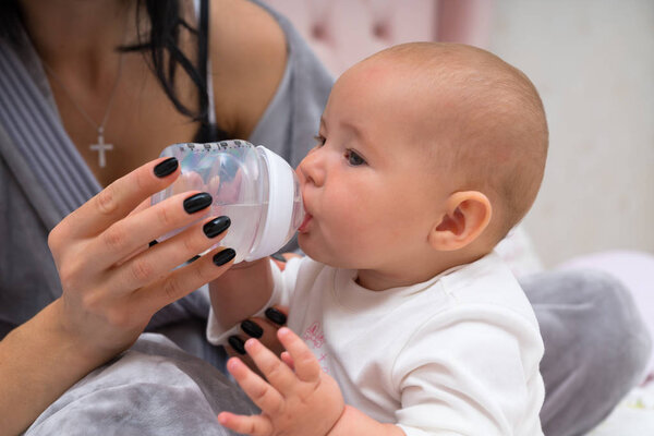 Mother feeding her cute little baby from a bottle in a close up view of the baby drinking