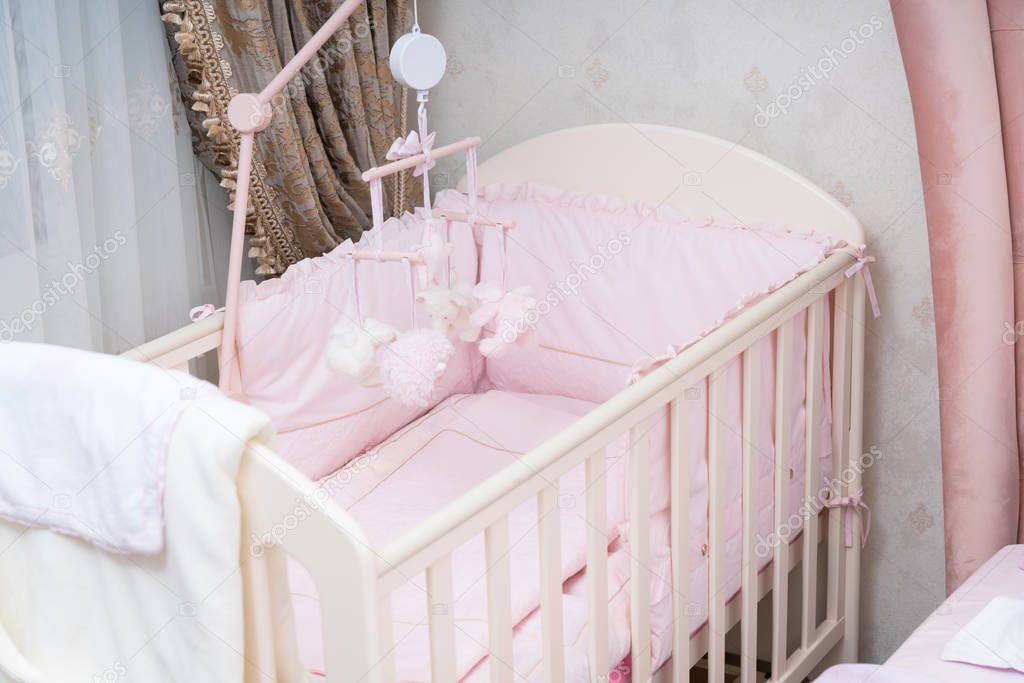 Empty white wooden cot fitted with pink linen in a nursery for a baby girl