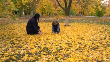 Genç kadın ve çocuk sonbahar park canlı akçaağaç yaprakları ile yere sarı yaprakları ile oynarken sıcak ceketler