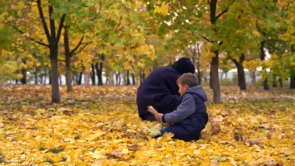 Jeune femme et adolescent jouant avec des feuilles jaunes sur le sol dans le parc en automne, jetant des poignées de feuilles haut 