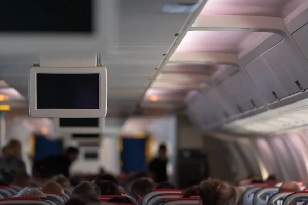 Airplane cabin full of passengers during a flight viewed from the back with a view to the overhead television screens