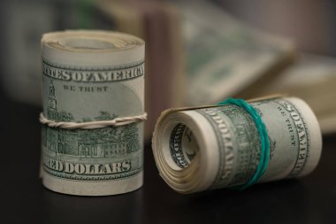 Two rolls of rolled USD bills tied with rubber bands one upright and one on its side on a black table in a conceptual financial or corruption image clipart