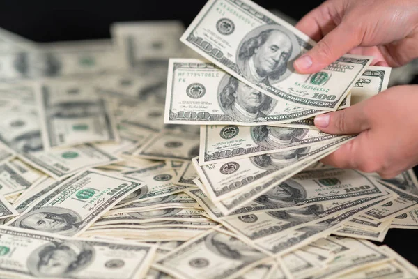 Person counting out their winnings, earnings or a payment holding a handful of dollar banknotes and placing them onto a pile on a table