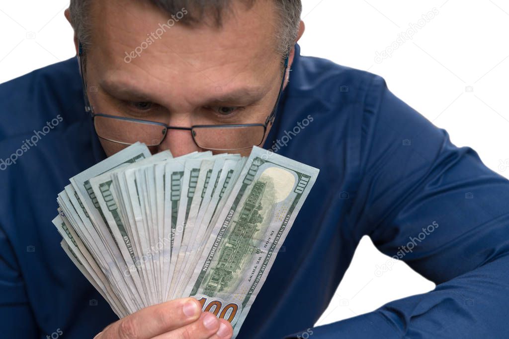 Thoughtful man holding a fanned handful of money with 100 USD banknotes looking down holding them in front of his face in a conceptual image