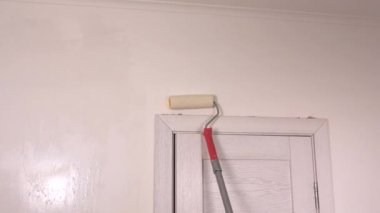 Beyaz bir duvarı rulo ile boyakan kişi