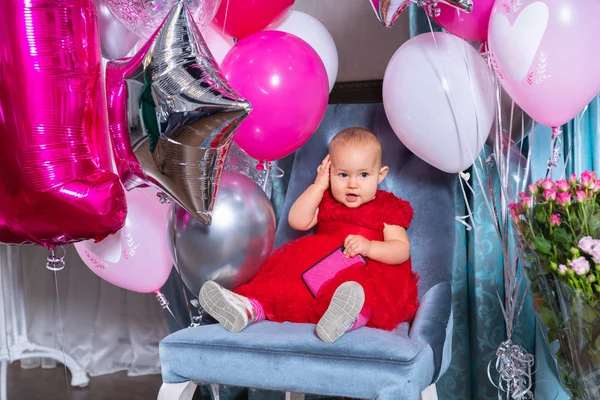 Schattige babymeisje op een stoel onder ballonnen — Stockfoto