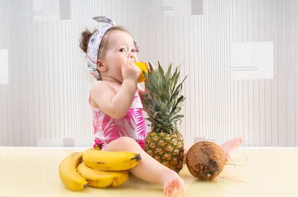 Niña sentada entre frutas, comiendo limón — Foto de Stock