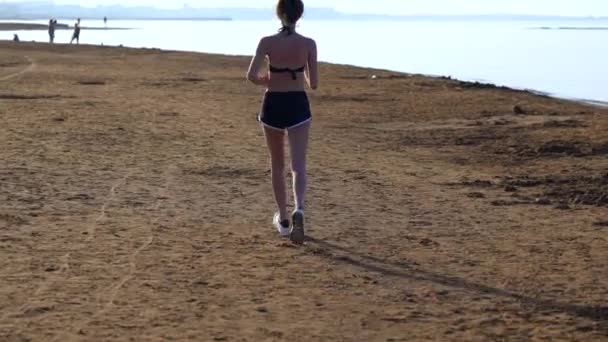 Подтянутая молодая женщина бегает по песчаному пляжу — стоковое видео