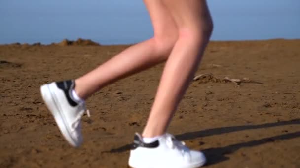 Νεαρή γυναίκα τρέχει σε μια αμμώδη παραλία — Αρχείο Βίντεο