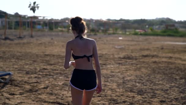 Slender young woman walking across a resort beach — Stock Video