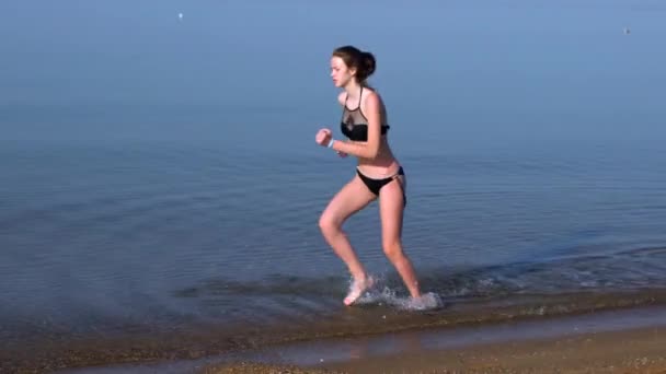 Smal ung kvinna som springer genom grunt hav — Stockvideo