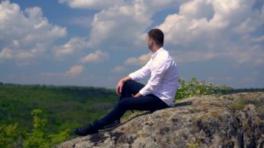 Ormanlık bir vadiye bakan genç adam oturuyor.