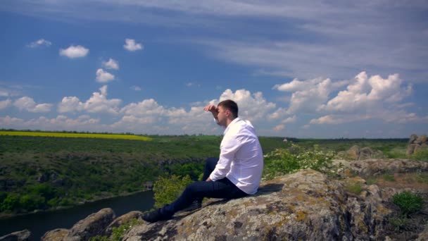 Jeune homme assis relaxant sur un rocher élevé — Video