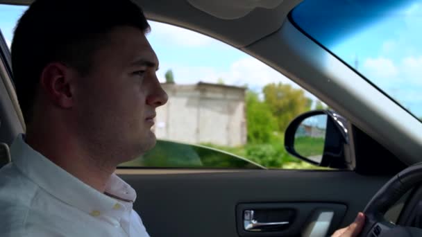 Молодой человек за рулем автомобиля, проезжающего мимо фермерских зданий — стоковое видео