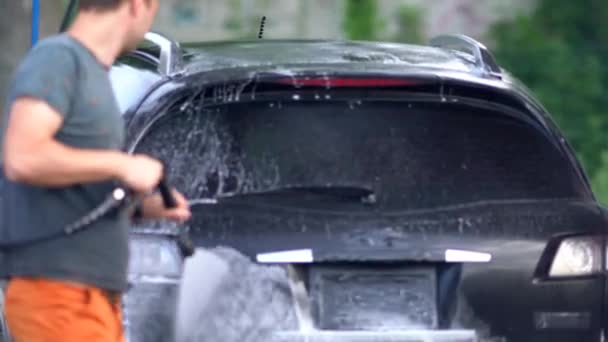 Jovem pulverizando seu carro com água ensaboada — Vídeo de Stock