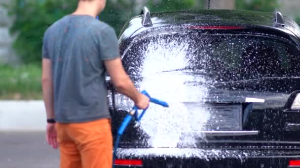 Joven rociando espuma en su coche en un lavado de coches — Vídeo de stock