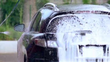 Sabunlu bir arabayı yıkayan genç adam.